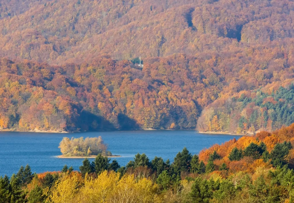 Jezioro Solińskie jesienią, otoczone kolorowym lasem i wzgórzami, z małą wysepką.