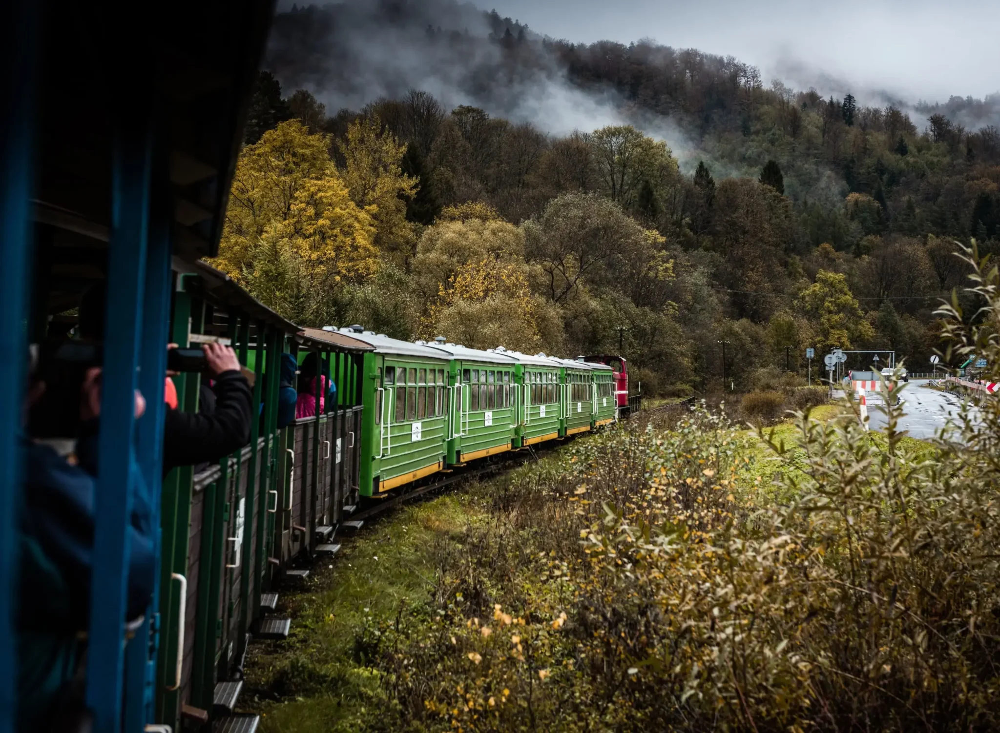 Zielona kolejka leśna jadąca przez malownicze bieszczadzkie lasy w jesiennej scenerii. Widoczne mgły unoszące się nad drzewami, podkreślające magiczny klimat regionu.