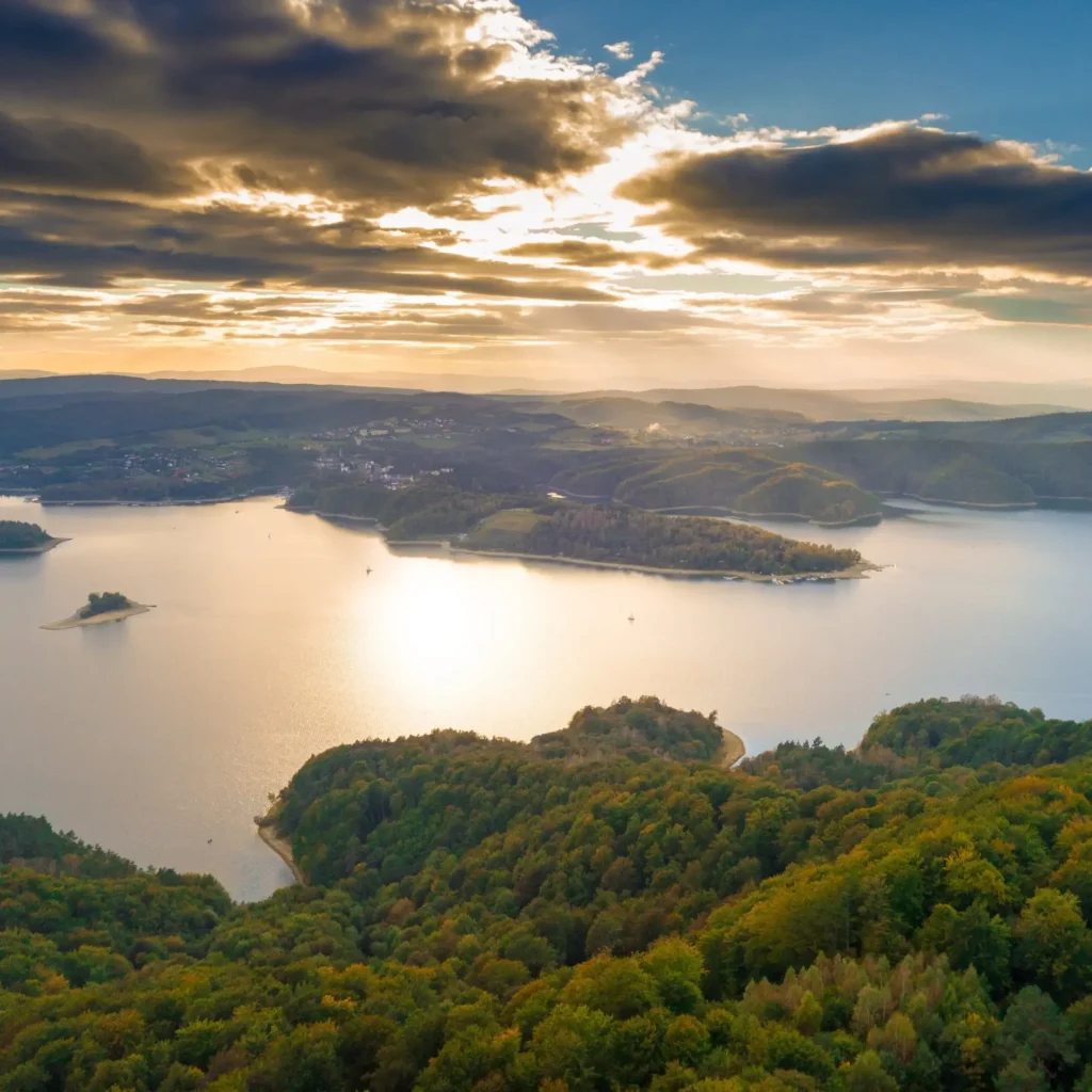 Malowniczy widok na Jezioro Solińskie otoczone wzgórzami, oświetlone promieniami zachodzącego słońca. Spokojna i romantyczna sceneria w sercu Bieszczad.