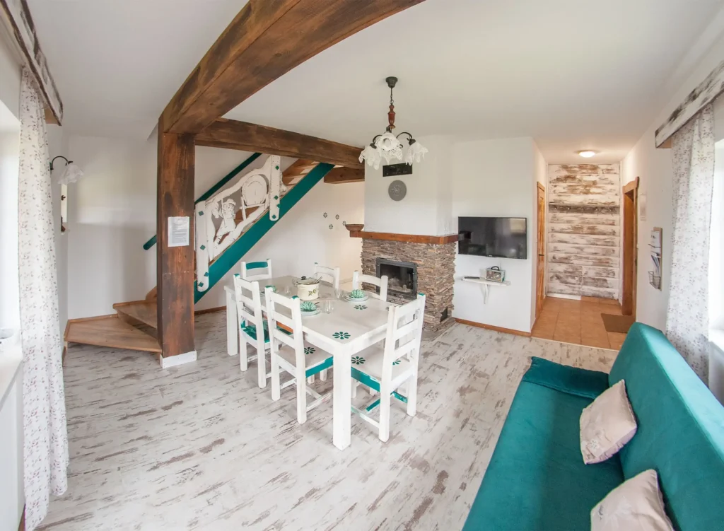 Salon z jadalnią w apartamencie Chata w Bieszczadzie, drewniane belki, białe meble i kominek, idealne miejsce na rodzinne spotkania w sercu Bieszczadów.