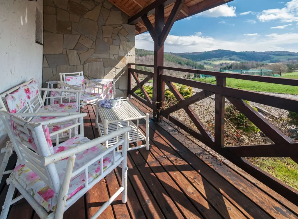 Balkon w apartamencie Chata w Bieszczadzie z białymi bambusowymi meblami, stolik kawowy i widok na zielone wzgórza Bieszczadów, idealne na poranny relaks.