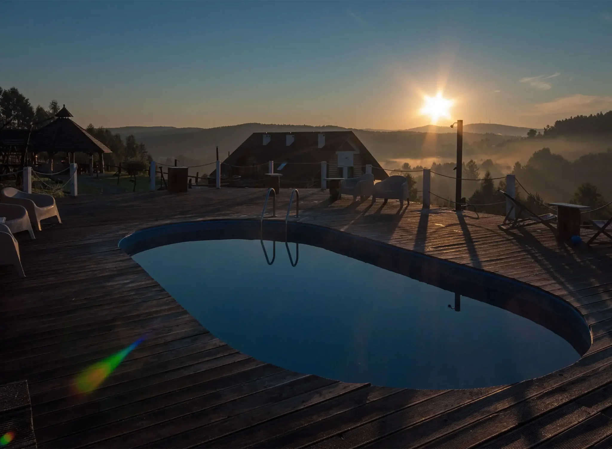 Basen na drewnianym tarasie w Chacie w Bieszczadzie o zachodzie słońca, z malowniczym widokiem na okoliczne wzgórza, idealne miejsce na relaks.