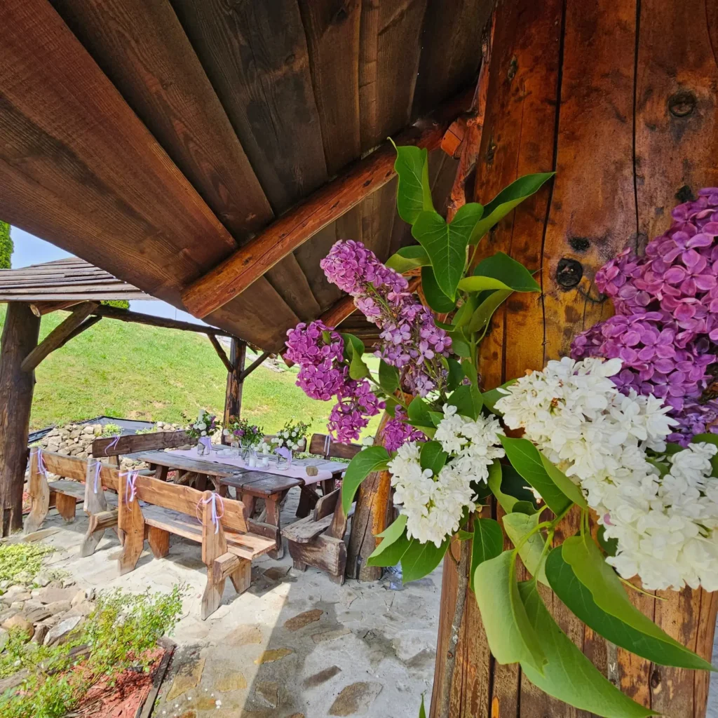 Drewniana chata grillowa z bukietami bzu w odcieniach bieli i fioletu, ozdobiona naturalnym wystrojem. Idealne miejsce na przyjęcia w Bieszczadach.