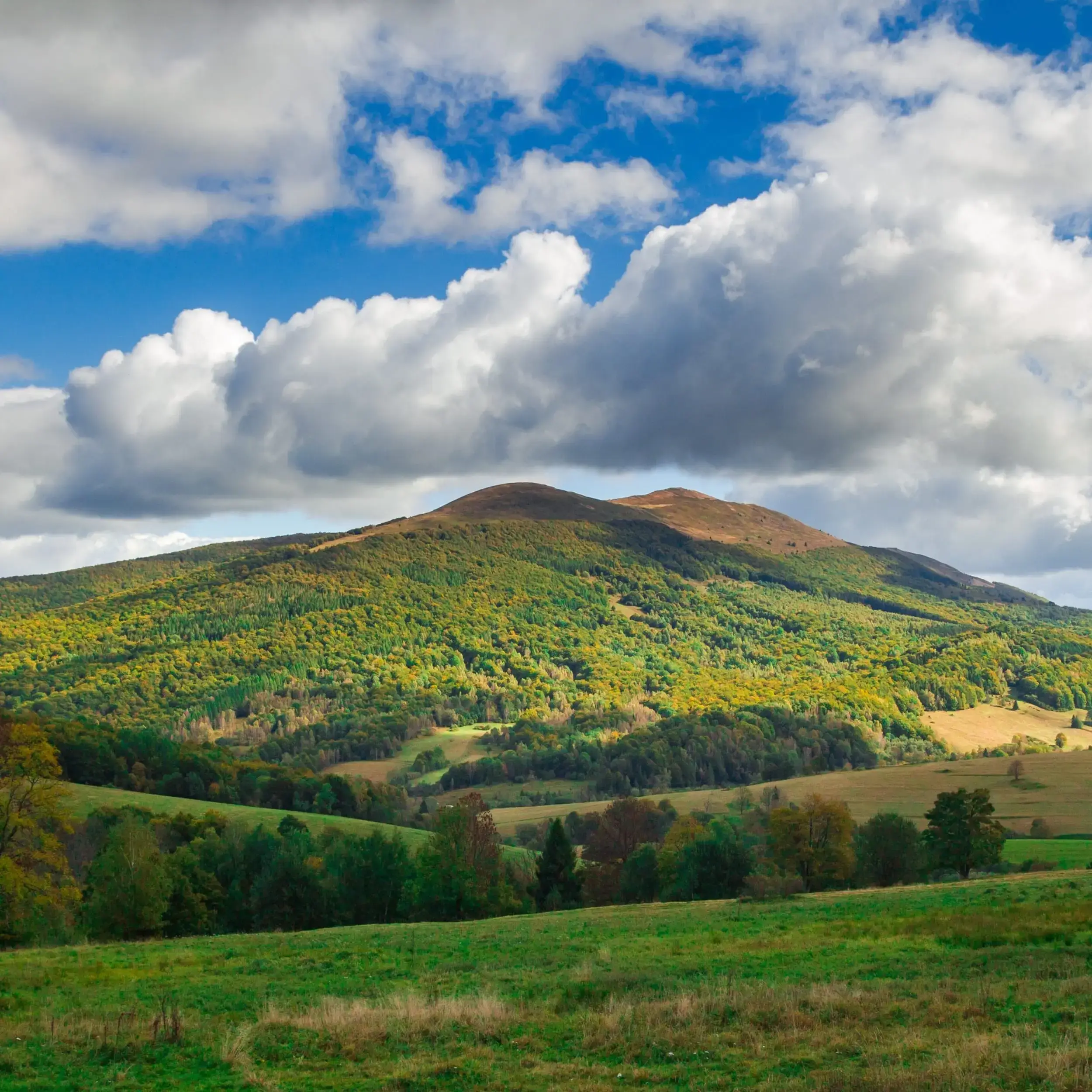 Zielone wzgórza Bieszczad wiosną z widokiem na połoniny i błękitne niebo ozdobione białymi chmurami. Idealne miejsce na majówkowy odpoczynek w otoczeniu natury.