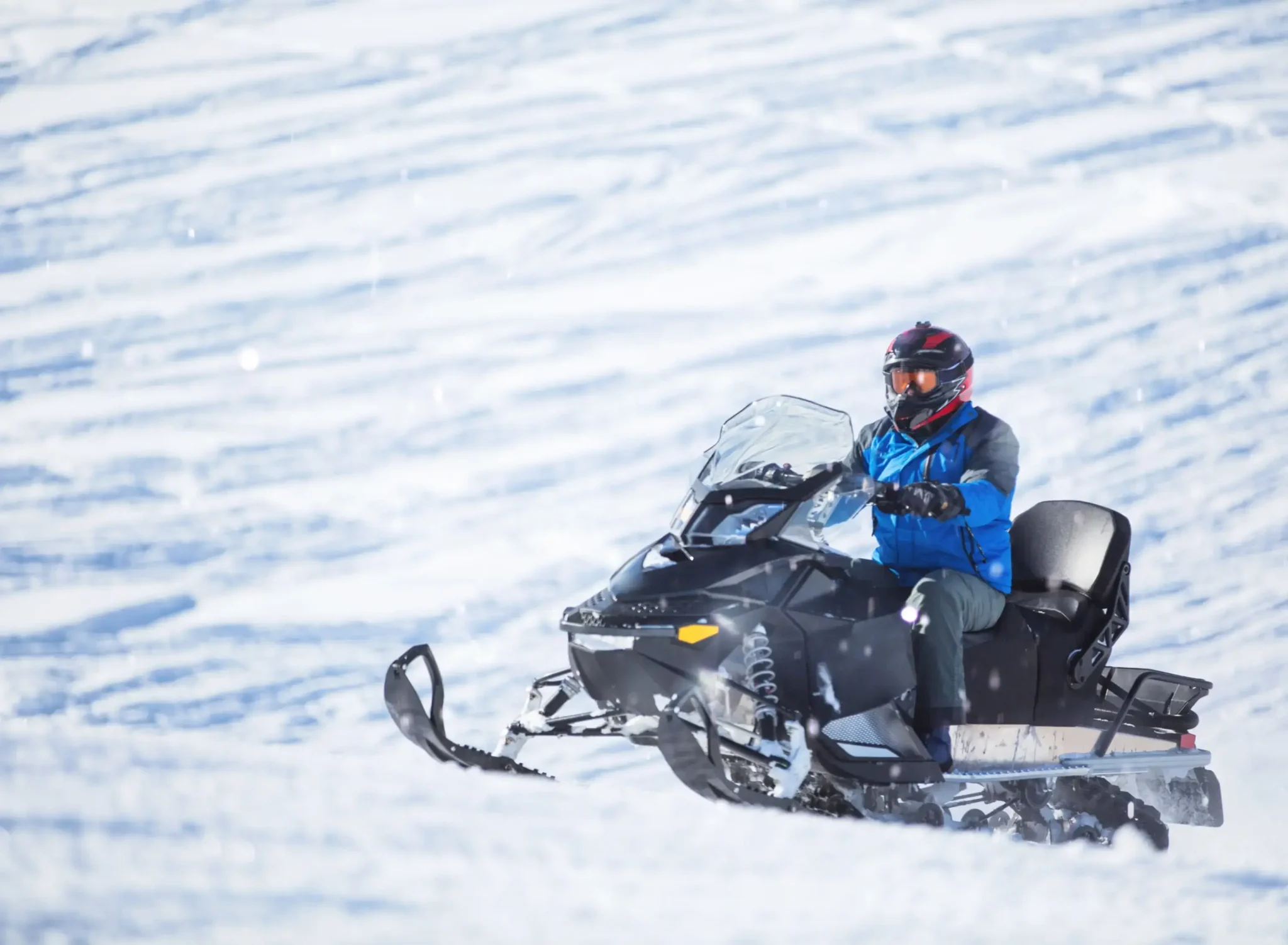 Mężczyzna w kasku i kurtce zimowej prowadzi skuter śnieżny na pokrytym śniegiem terenie w Bieszczadach. Adrenalina i zimowe przygody w malowniczym otoczeniu.