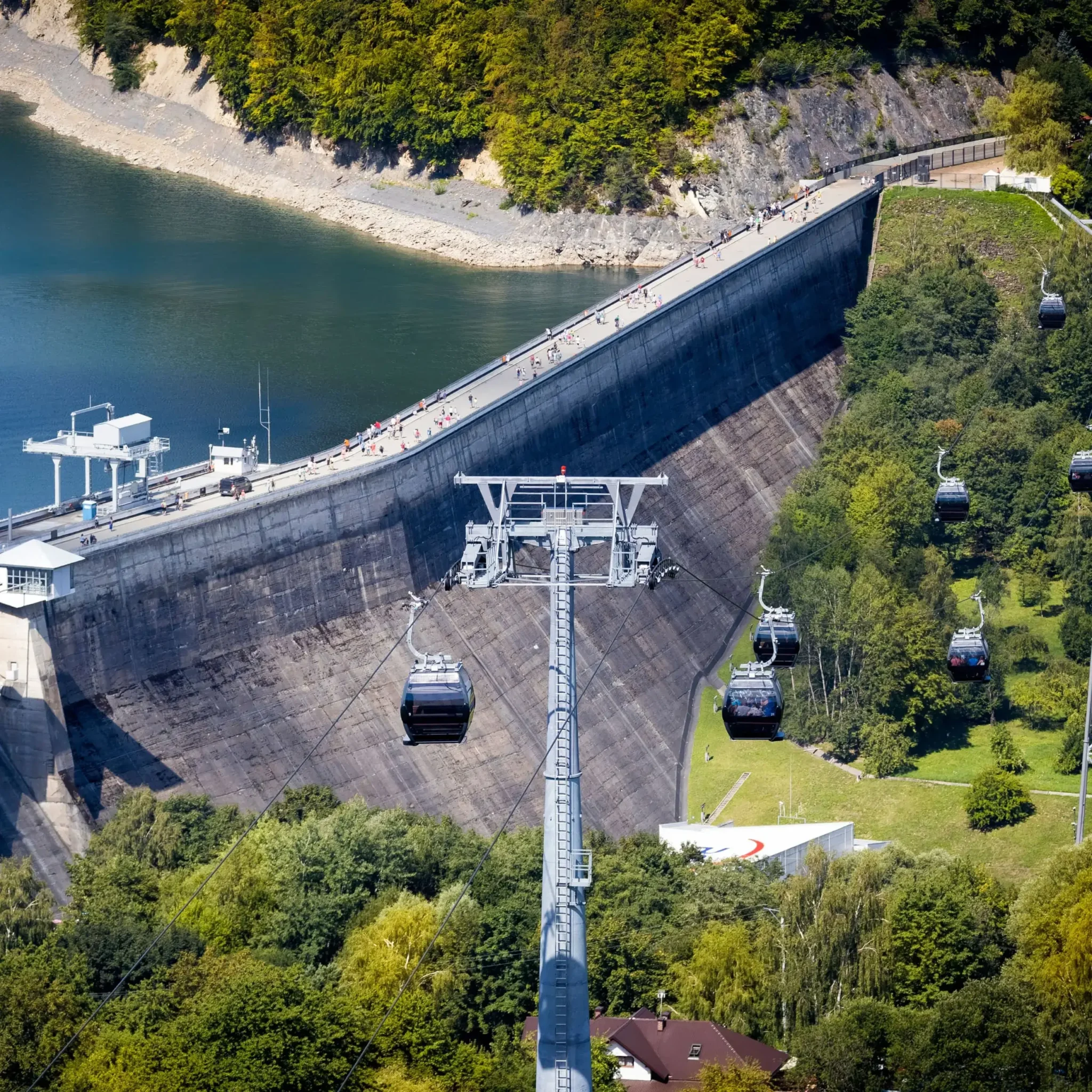 Widok na kolej gondolową prowadzącą nad zaporą w Solinie, otoczoną zielenią i turkusową wodą jeziora. Popularna atrakcja turystyczna w Bieszczadach.