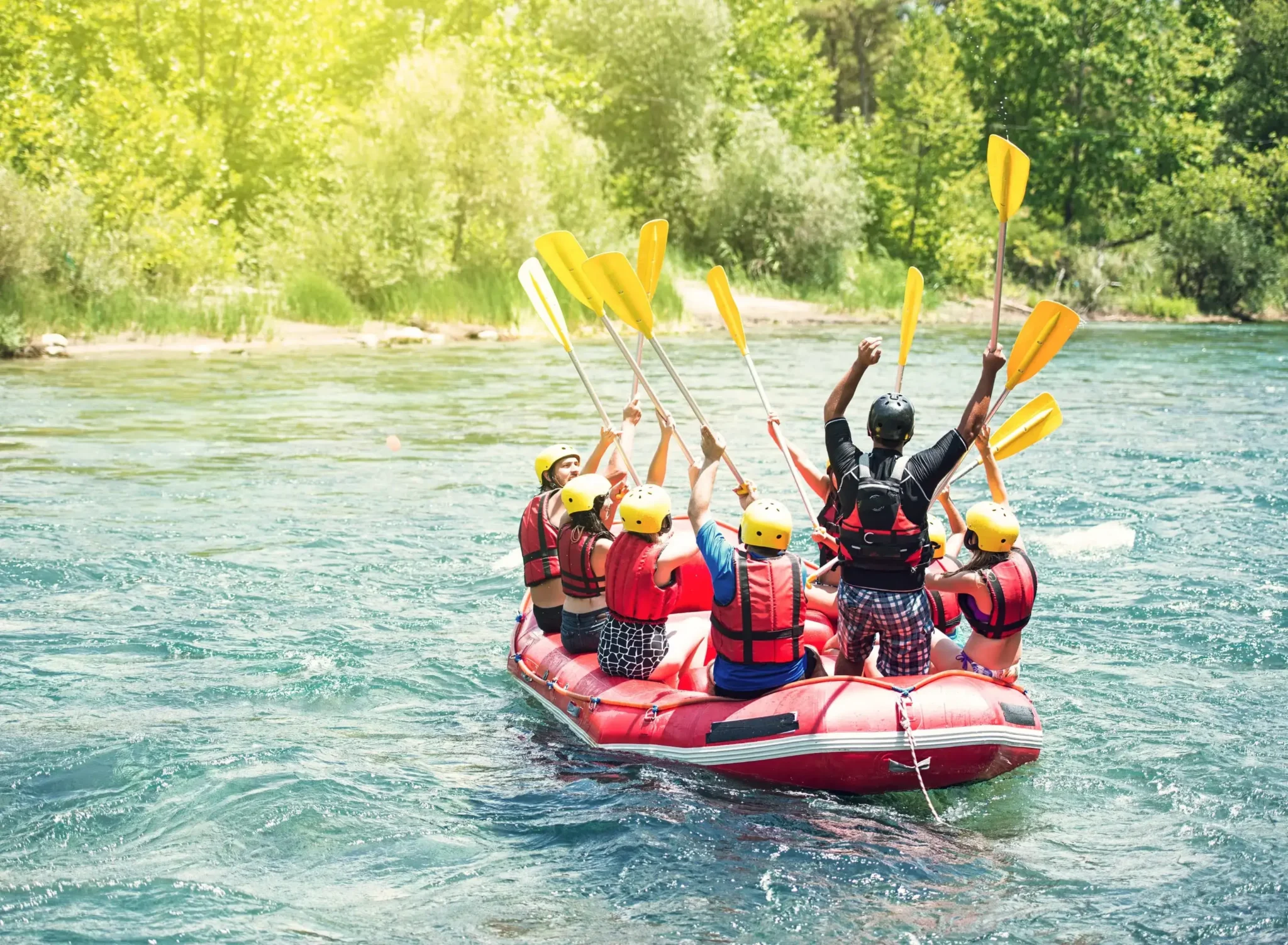 Grupa ludzi w kaskach i kamizelkach ratunkowych podczas raftingu na rwącej rzece w Bieszczadach. Przyroda, adrenalina i zespołowe przeżycia w pięknym otoczeniu zieleni.
