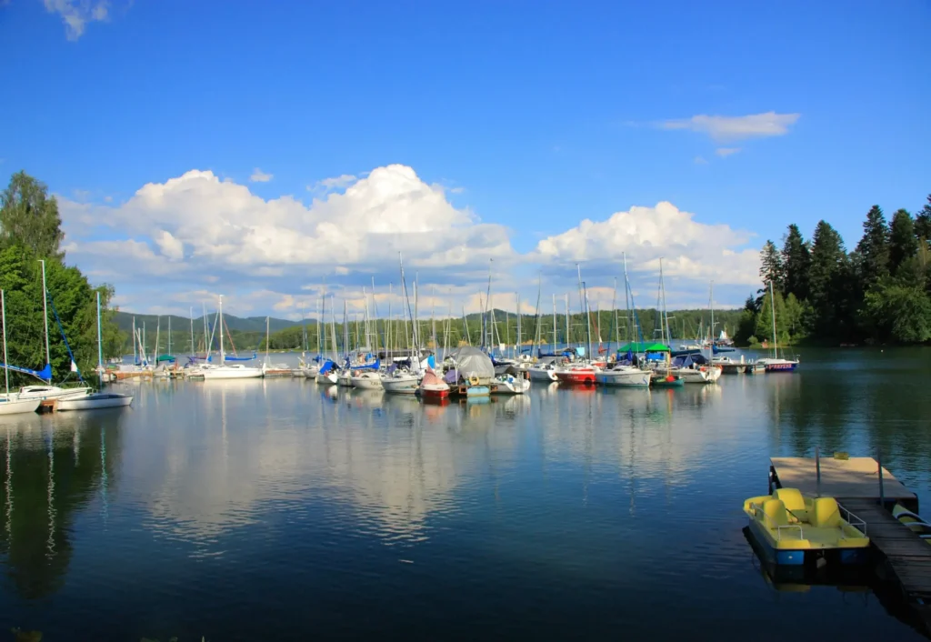 Jezioro Solińskie w Bieszczadach, z przystanią pełną jachtów i łodzi żaglowych, otoczone lasami i wzgórzami.