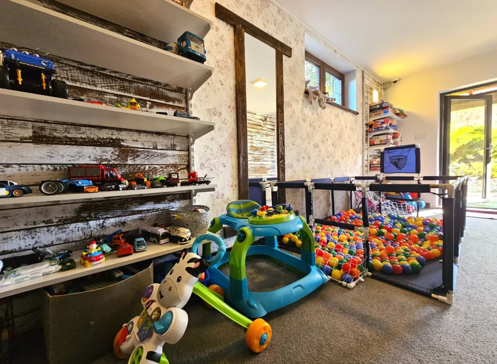 Pokój zabaw dla dzieci w Bieszczadach, wyposażony w zabawki, basen z piłeczkami oraz regał z modelami samochodów.