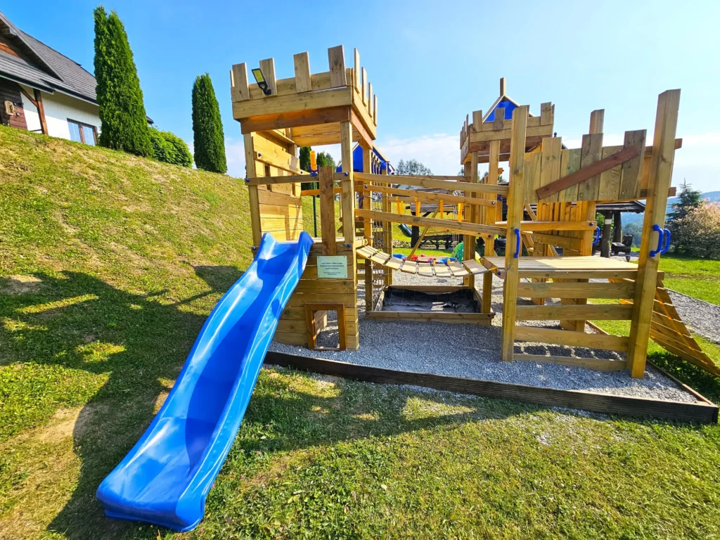 Drewniany plac zabaw ze zjeżdżalnią i mostkiem linowym na zielonym wzgórzu w Bieszczadach