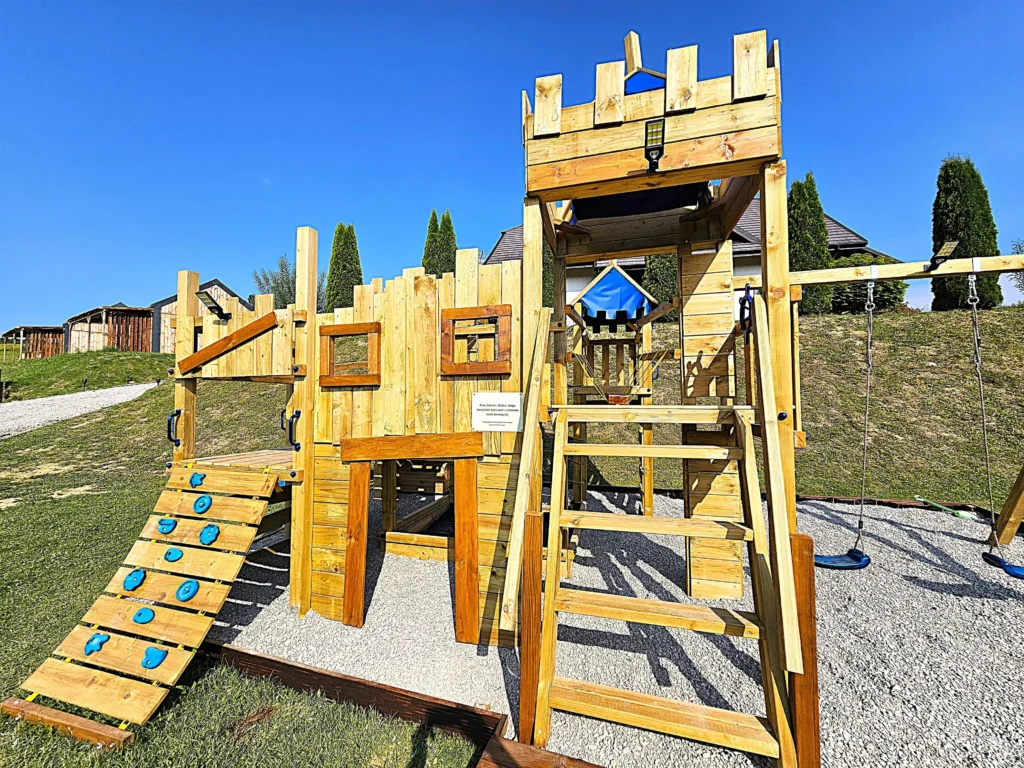 Duży drewniany plac zabaw z wieżyczkami, drabinką, huśtawkami i ścianką wspinaczkową w Bieszczadach