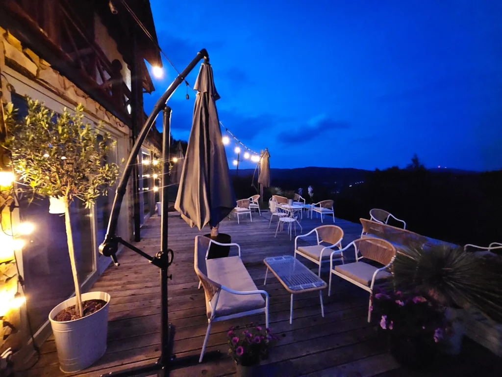 Drewniany taras z lampkami i widokiem na wzgórza o zmroku, przy Chacie w Bieszczadzie