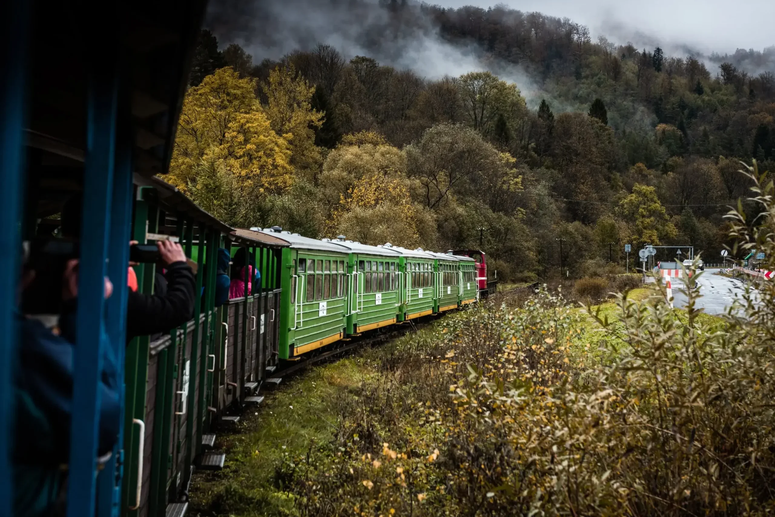 Zielona kolejka leśna jadąca przez malownicze bieszczadzkie lasy w jesiennej scenerii. Widoczne mgły unoszące się nad drzewami, podkreślające magiczny klimat regionu.