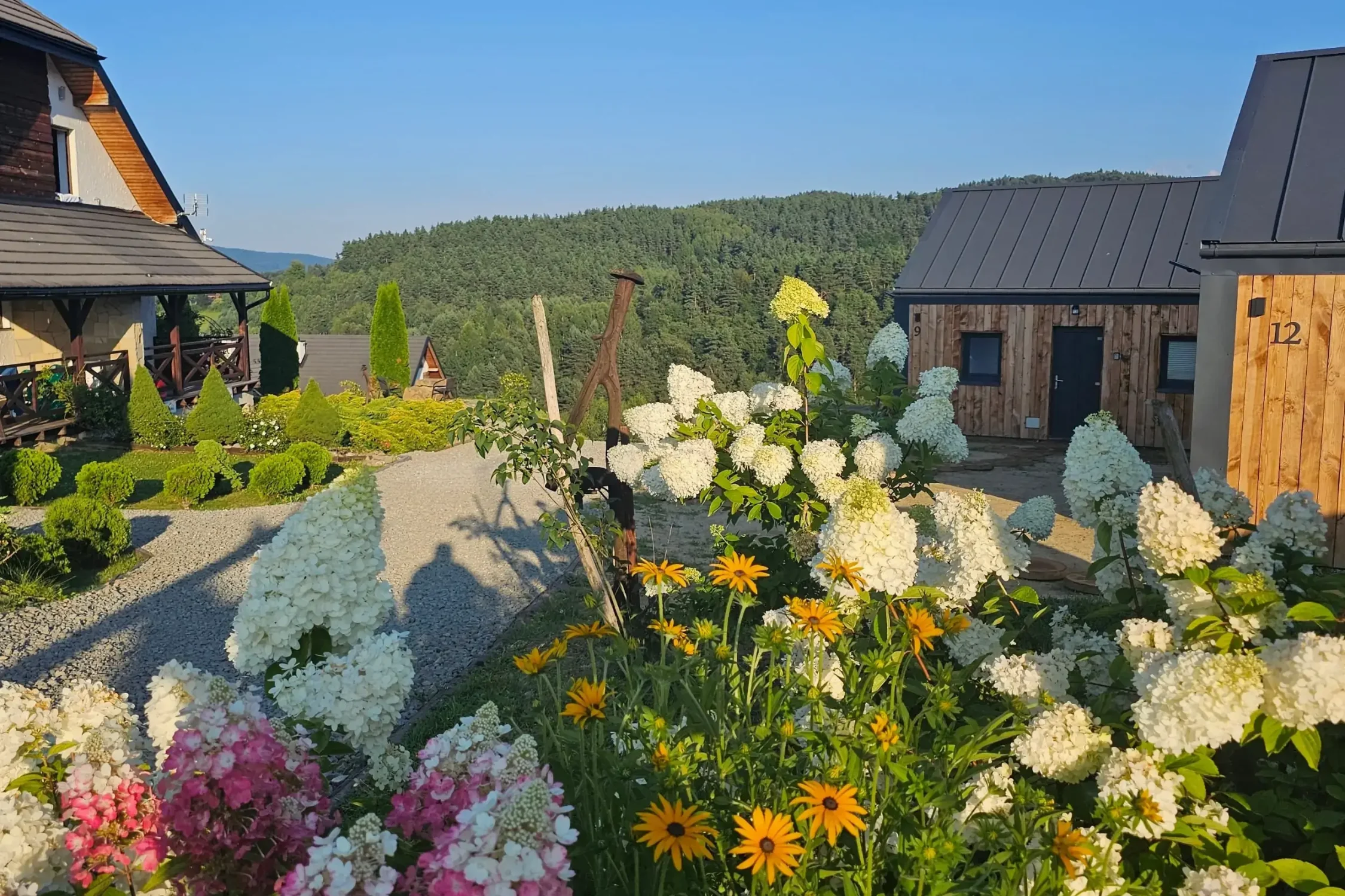 Ogród w pełnym rozkwicie z kolorowymi kwiatami na tle bieszczadzkich wzgórz i drewnianych domków. Idealne miejsce na wiosenny wypoczynek.
